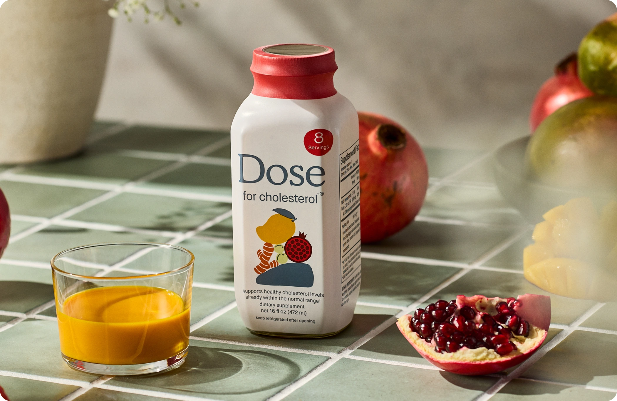 Dose cholesterol supplement bottle with a glass of the drink and pomegranate on a tiled surface.